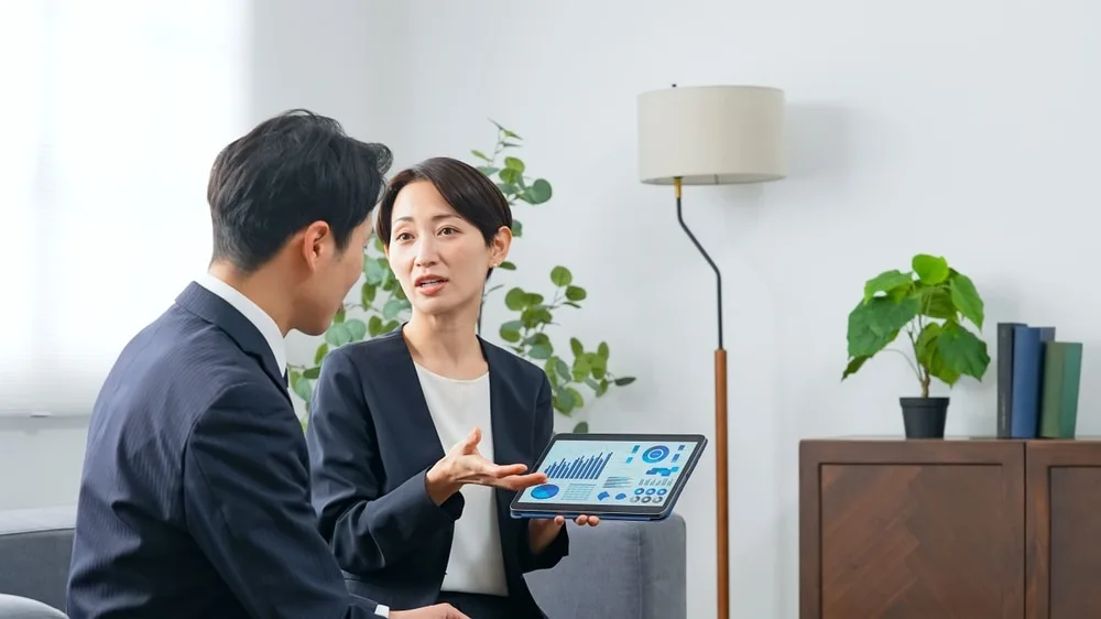 ビジネスウーマンがタブレットの売上グラフをビジネスマンに説明している