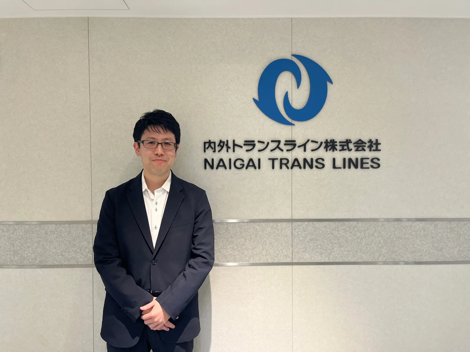 内外トランスラインの社名壁前に立つ男性
