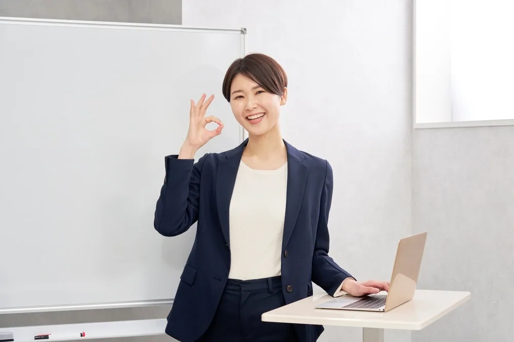 ビジネスウーマンがノートパソコンの前でOKサインを示す様子