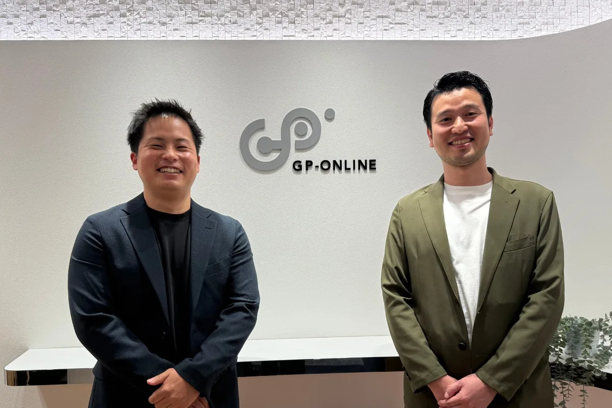 GP-ONLINEのロゴ背景で並ぶ2人の男性社員