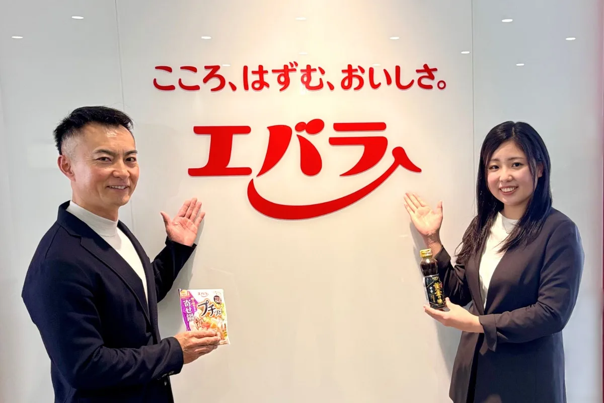 エバラ食品の社員が商品を持ち、ロゴの前で手を挙げている