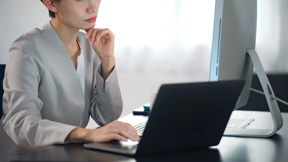 ノートパソコンを操作しながら考える女性営業担当者
