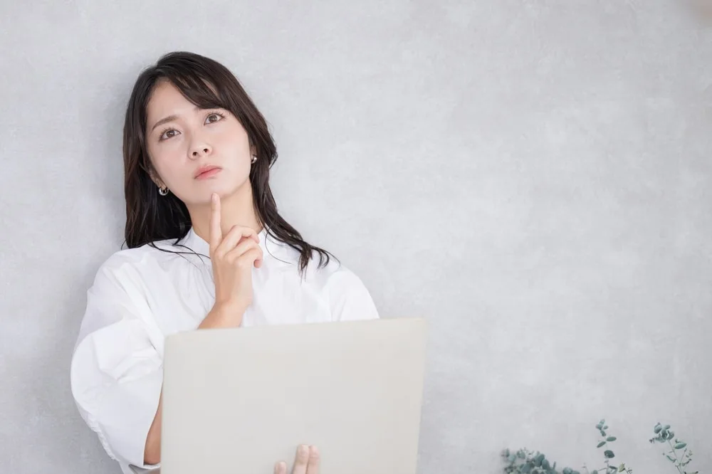 白いシャツの女性がノートパソコンを持ち上を見つめる