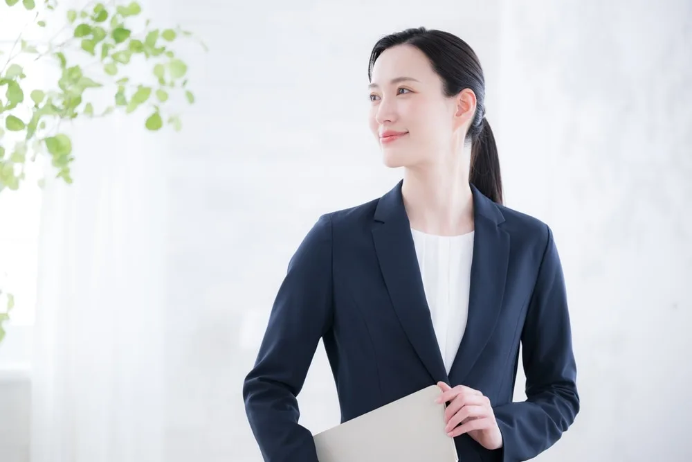 ビジネススーツの女性がタブレットを持ち窓辺に立つ