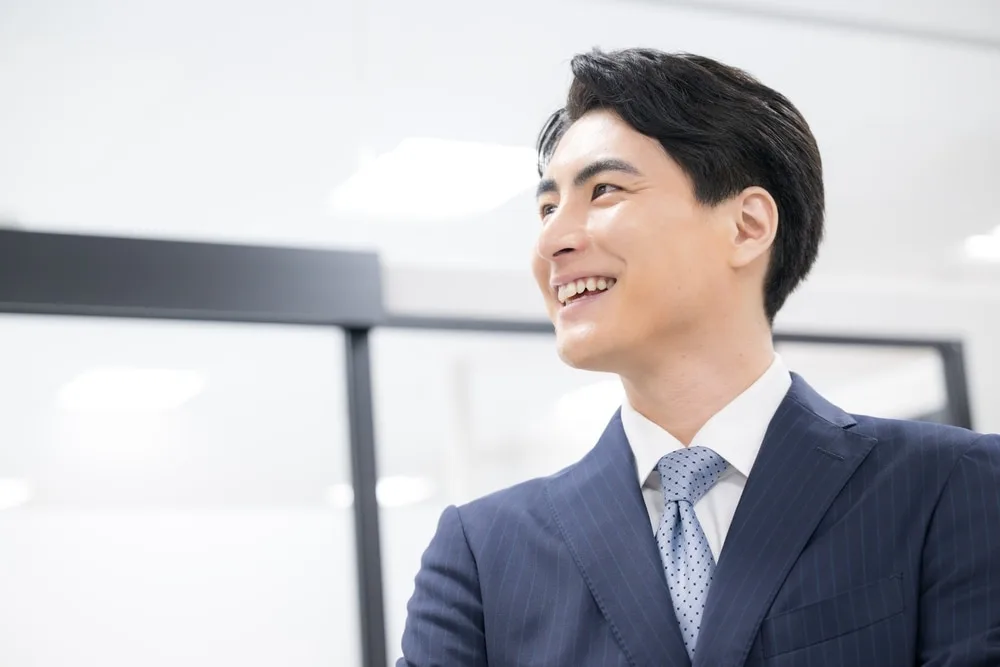 紺色のスーツとネクタイの男性がオフィスで笑顔で上を見ている
