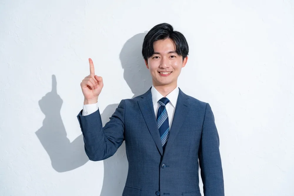ビジネススーツ姿の男性が人差し指を立てて笑顔で上を指している