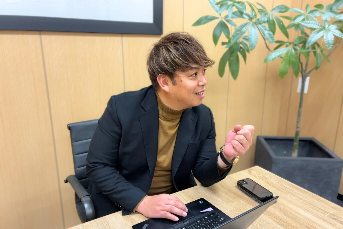 机の上のキーボードを前に、身振りを交えて説明する会社員