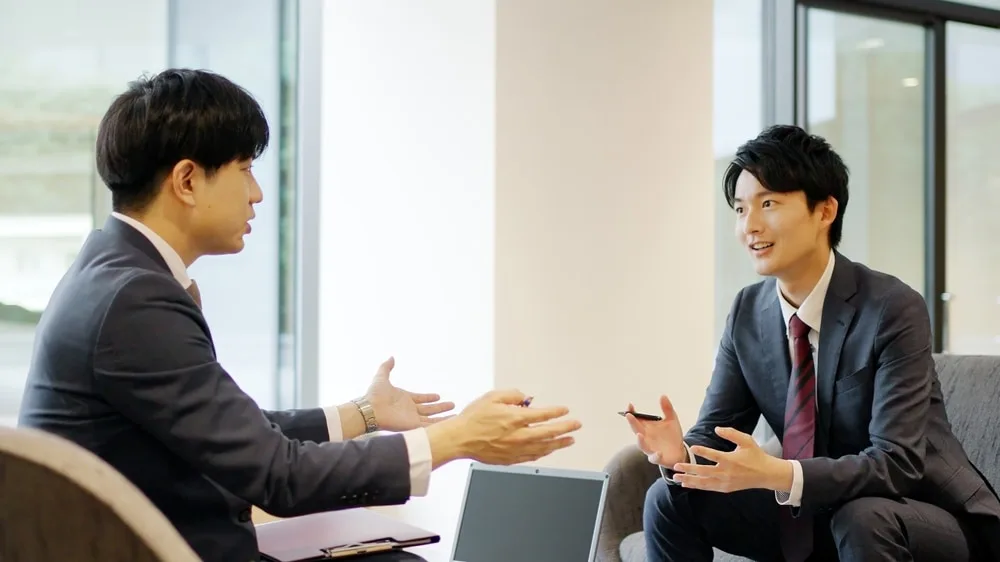 ビジネススーツの2人の男性がノートパソコンを前に対面で会話