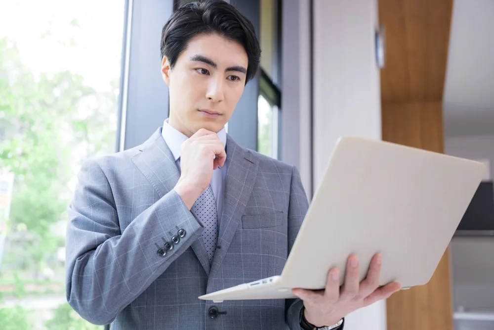 ノートパソコンを持って考える営業職の男性