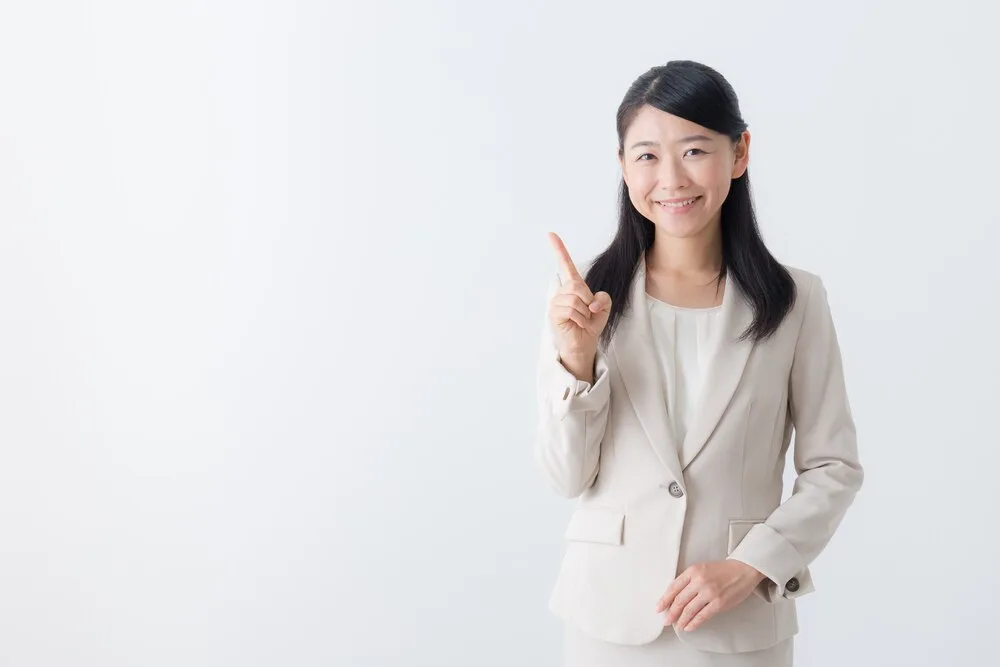 ベージュのスーツを着た女性が人差し指を立てポーズ
