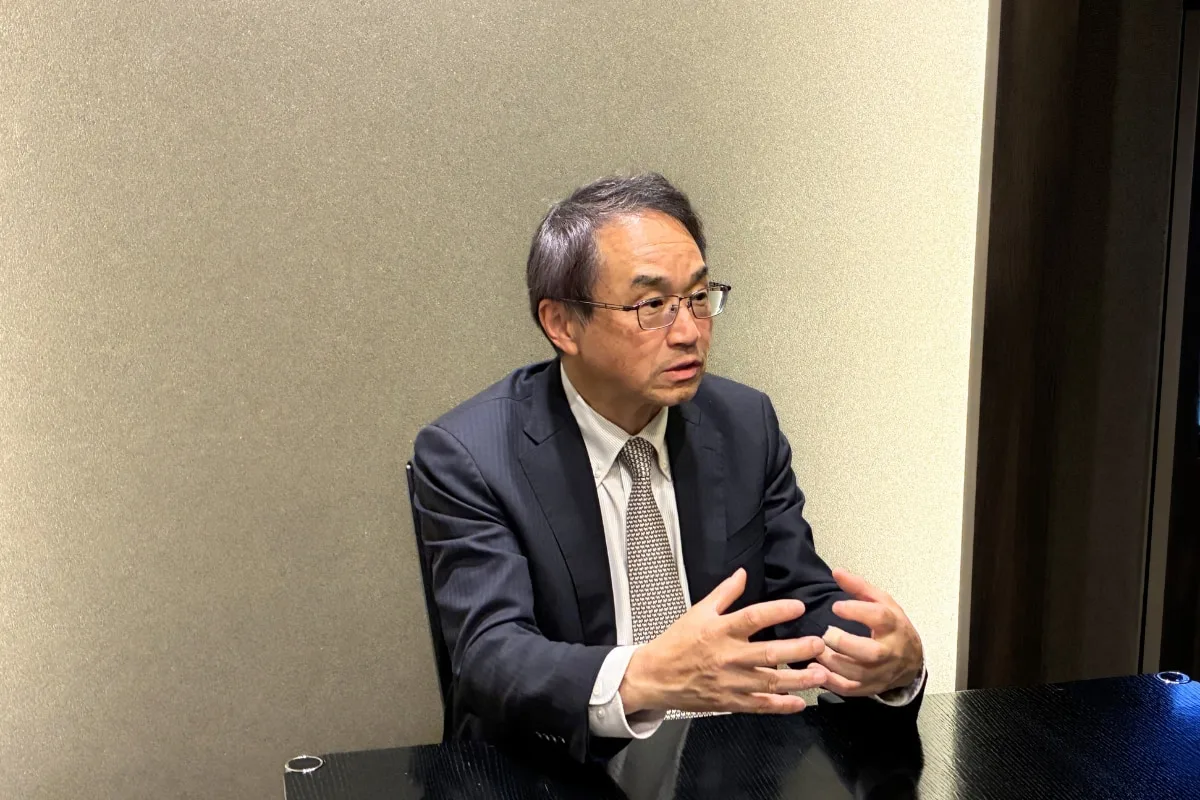 眼鏡をかけた男性が紺色スーツで身振りを交えて説明している